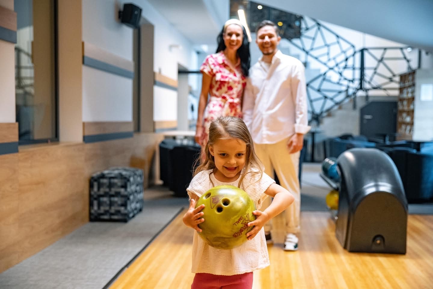 Dievčatko s bowlingovou guľou a rodičia v pozadí — rodinná zábava Happy Heads